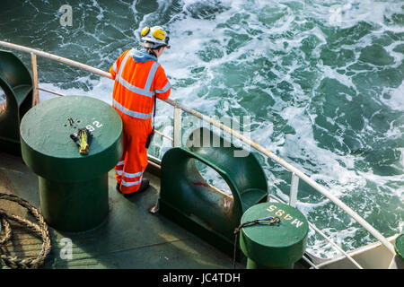 Female crew member in orange overall and wearing safety helmet working on deck of car carrier / cargo ship at sea Stock Photo