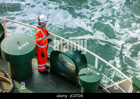 Female crew member in orange overall and wearing safety helmet working on deck of car carrier / cargo ship at sea Stock Photo