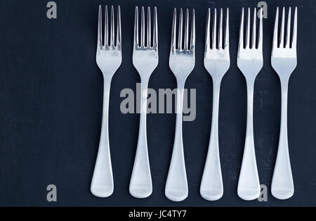 Five steel dinner forks in a row on black board background Stock Photo