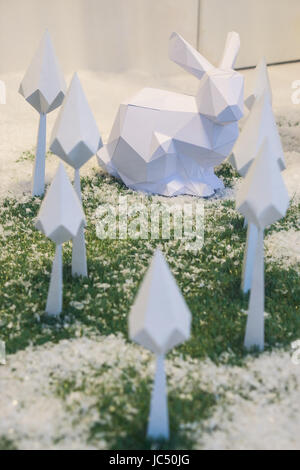 Christmas winter origami. white rabbit and white paper trees on green grass covered with snow Stock Photo