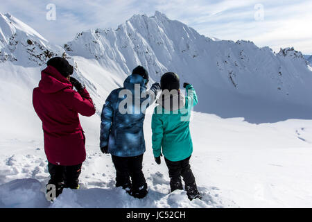 Professional Snowboarders, Helen Schettini, Robin Van Gyn and Jamie Anderson, look at lines they prepare to ride on a snowboarding trip to Haines, Alaska. Stock Photo
