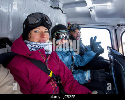 Professional snowboarders Helen Schettini, Robin Van Gyn, and their filmer ride in a helicopter on the way to snowboard on a sunny day in Haines Alaska. Stock Photo