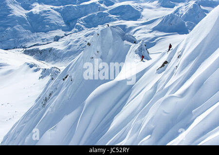 Professional Snowboarder Marie France Roy, Robin Van Gyn, and Helen Schettini, stand on top of a mountain and get ready to drop in on their snowboards after being dropped off by a helicopter on a sunny day in Haines, Alaska. Stock Photo