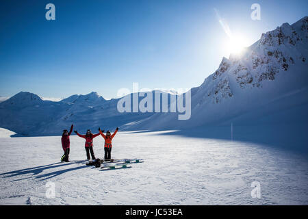 Professional snowboarders, Robin Van Gyn, Marie France Roy, and Helen Schettini throw their hands up in excitement after a fun run on a sunny day in Haines, Alaska. Stock Photo