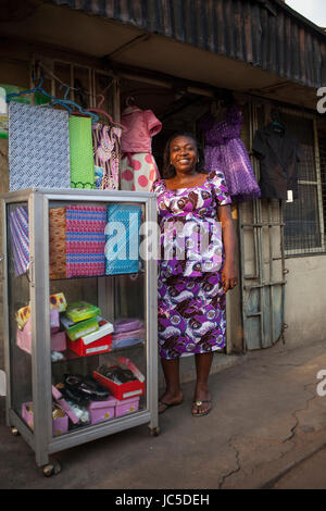 A female shop keeper poses outside her shop with her fabric, Nigeria, Africa Stock Photo