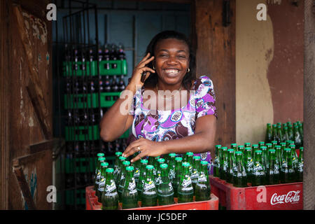 A female shop keeper poses outside her shop with bottles of drink, Nigeria, Africa Stock Photo
