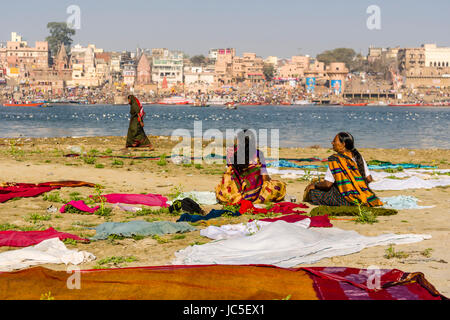 Two women are sitting on the sand banks at the holy river Ganges, waiting for their laundry to dry, panorama of Dashashwamedh Ghat, Main Ghat, in the  Stock Photo