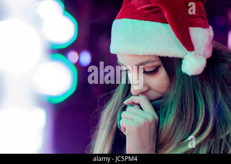 Sad woman by the christmas tree contemplating. Lonely Christmas woman on the winter street at night. Festive brunette feeling sad at christmas looking Stock Photo