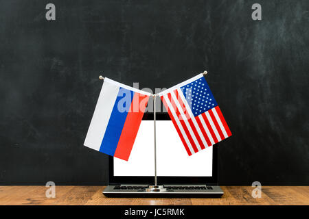 Concept of hacking into the computer of American and Russian political problem flag on flagpole in front of black chalkboard with copy space. Stock Photo