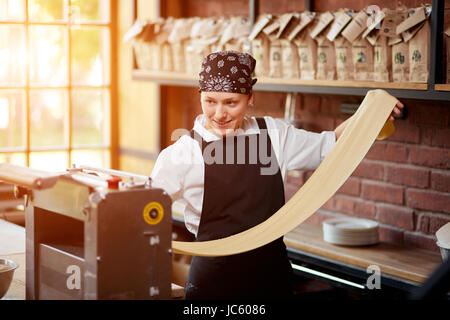 Woman cooks dough on machine for making pasta Stock Photo