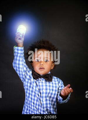 Little genius with illuminated lamp in hand isolated on black background, african boy is a great physics, back to school concept Stock Photo