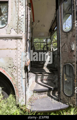 Worn drivers seat and steering wheel in front of abandoned commuter bus with open door. Stock Photo