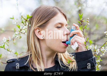 Picture of a young woman having pollen allergy, holding a bronchodilator outdoor Stock Photo