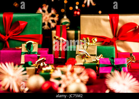 Many plain Christmas presents piled up on a red cloth. All with unicolored bows in red, green and gold. Narrow depth of field resulting in bokeh. Blurred ornaments and stars in front and back. Stock Photo