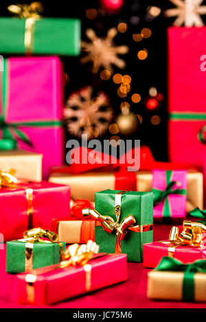 Many plain Christmas gifts arranged on a red cloth. Narrow depth of field. Mostly soft shapes in vibrant colors. Defocused straw stars and baubles over black background. Focus on central green box. Stock Photo