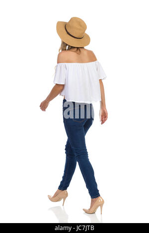 Casual woman in straw hat, jeans, white shirt walking. Rear side view. Full length studio shot on isolated on white. Stock Photo
