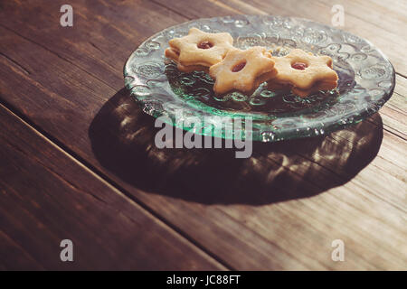 Jam filled cookies on a glass plate on wooden table in the morning light Stock Photo