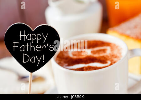 closeup of a black heart-shaped signboard with the text happy fathers day written in it and a cup of cappuccino with a pair of eyeglasses and a mousta Stock Photo