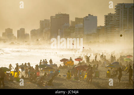 RIO DE JANEIRO - MARCH 20, 2017: Silhouettes of people enjoing the golden misty sunset shores of Ipanema Beach in Rio de Janeiro, Brazil Stock Photo