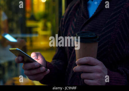 Close up of a businessman using mobile phone and holding paper cup. Close-up detail of a businessmans hand holding paper cup and using a smartphone wh Stock Photo