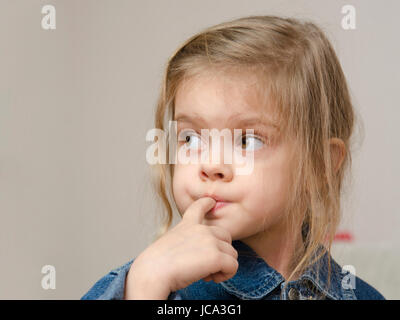 Four-year-old girl stuck her index finger in her mouth and enthusiastically looking left. Girl dressed in a denim jacket. Portrait Stock Photo