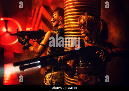 Two women with big guns war fighting thriller concept. Dark red dramatic light and urban interior. Stock Photo