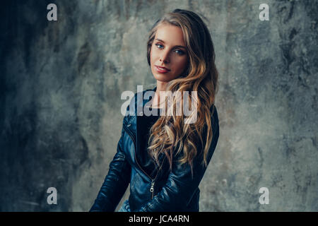 Young positive woman in leather jacket portrait on stone wall background