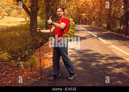 Young man tourist walking with sticks on road and showing thumbs up handsign Stock Photo