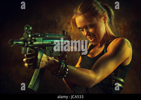 Young strong woman with big gun in dramatic urban interior. Tattoo on body. Stock Photo