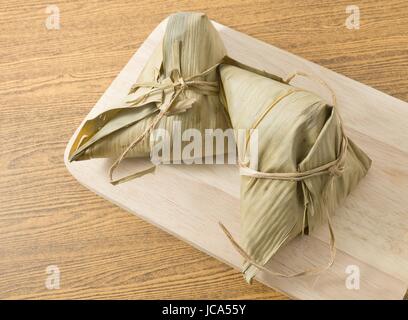 Chinese Cuisine, Two Zongzi or Sticky Rice Dumpling on Wooden Board for Dragon Boat Festival. Stock Photo