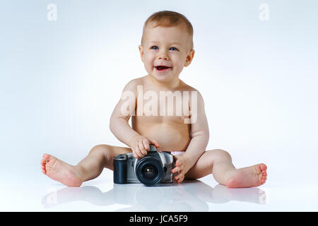 Eight month baby trying to be photographer and playing with camera on white background with reflection Stock Photo