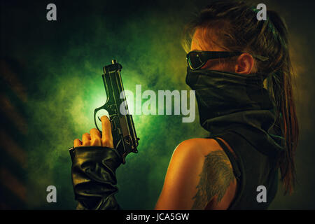 Dangerous woman fighter with gun and scarf in dark interior with smoke. Tattoo on body. Stock Photo