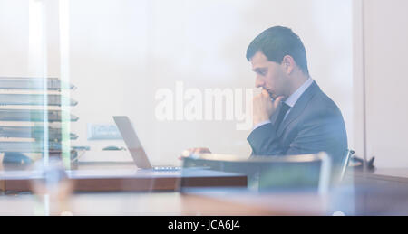 Elegant businessman analyzing data on laptop computer in modern office. Stock Photo