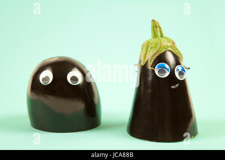 Minimal still life photography.An aubergine cut in half. Each part, wearing doll's eyes represents a man and a woman. Dredge scene on a pop colored ba Stock Photo