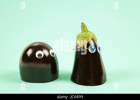 Minimal still life photography.An aubergine cut in half. Each part, wearing doll's eyes represents a man and a woman. Dredge scene on a pop colored ba Stock Photo