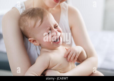Young woman with crying baby on hands. Bright white colors. Stock Photo