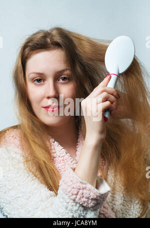 Young blond woman in bathrobe comb hair after washing. On white background. Stock Photo