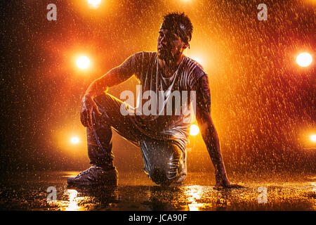 Young man break dancing in club with lights, water and smoke. Tattoo on body. Stock Photo