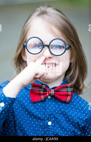 funny portrait of boy with bow tie and big glasses picking his nose Stock Photo