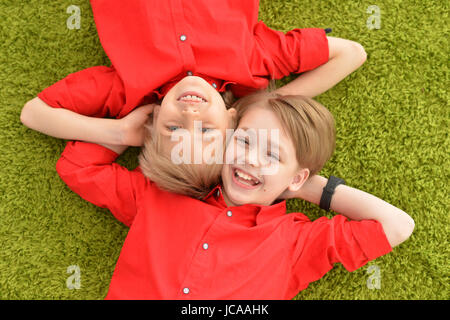 Two smiling boys in red shirts lying on floor with green carpet Stock Photo