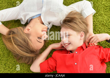 Smiling mother and son lying on floor with green carpet Stock Photo