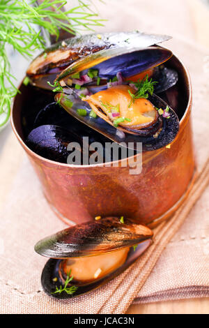 Delicious freshly boiled marine mussels in a copper saucepan with their shells open garnished with dill for a gourmet seafood starter, high angle closeup view Stock Photo