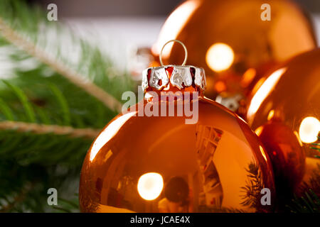 Glänzende orangene Glaskugeln Weihnachtskugeln mit grünen Zweigen auf einem Jutesack als Nahaufnahme Stock Photo