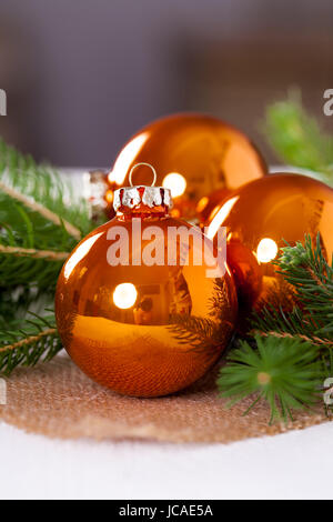 Glänzende orangene Glaskugeln Weihnachtskugeln mit grünen Zweigen auf einem Jutesack als Nahaufnahme Stock Photo