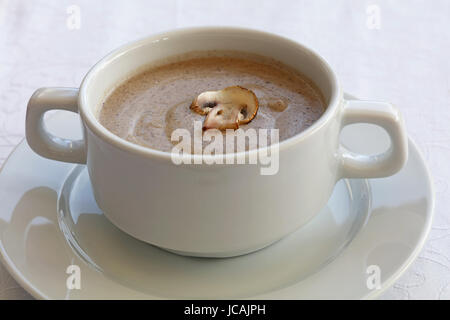 Portion of champignon mushroom cream soup in white porcelain tureen pot on the table, close up, high key, high angle view Stock Photo