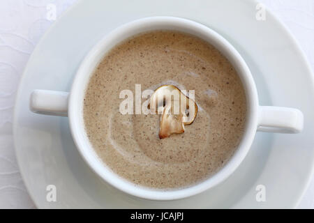 Portion of champignon mushroom cream soup in white porcelain tureen pot on the table, close up, high key, elevated top view Stock Photo