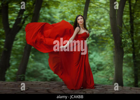 The girl is in the forest, her red dress develops wind. She stands on the precipice. Stock Photo