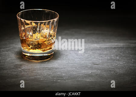 Whiskey on the rocks in a glass tumbler standing on a bar counter in the shadows with a highlight over copyspace or a place for product placement Stock Photo