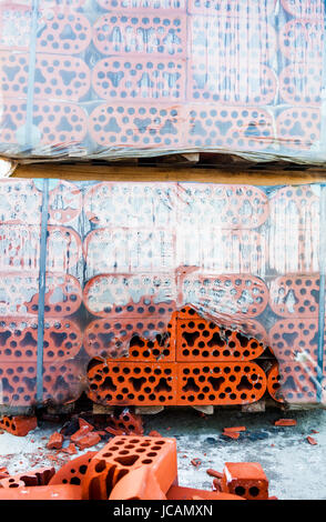 Stack of new silicate bricks in misted polyethylene with the pile of beaten bricks nearby. Stock Photo
