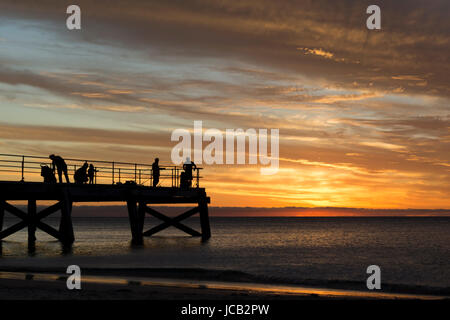 Sillouetted people fishing off the end of the Normanville Jetty, South Australia at sunset. This area is in the Fleurieu Peninsula. Stock Photo